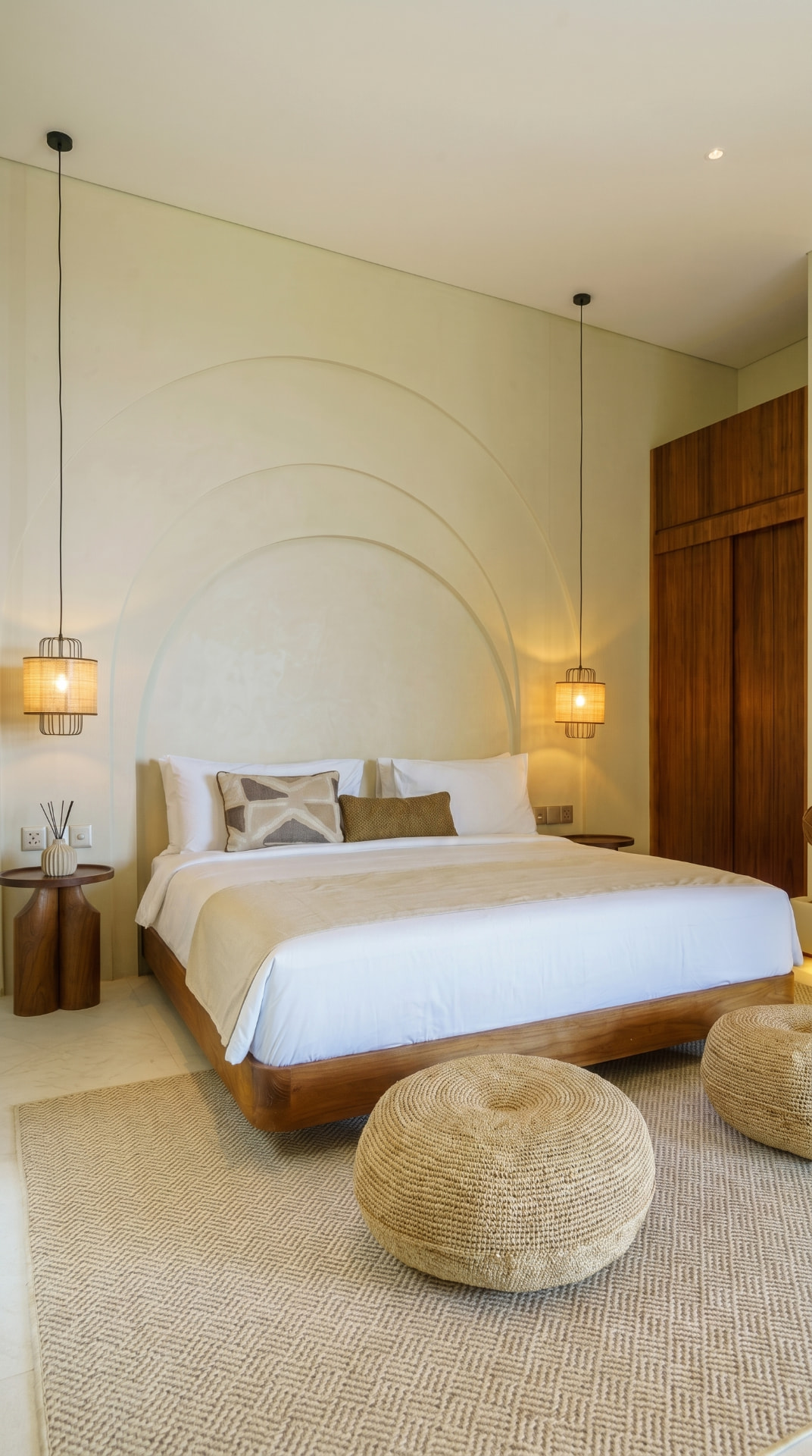 Empty villa bedroom with arched headboard and rattan pendants